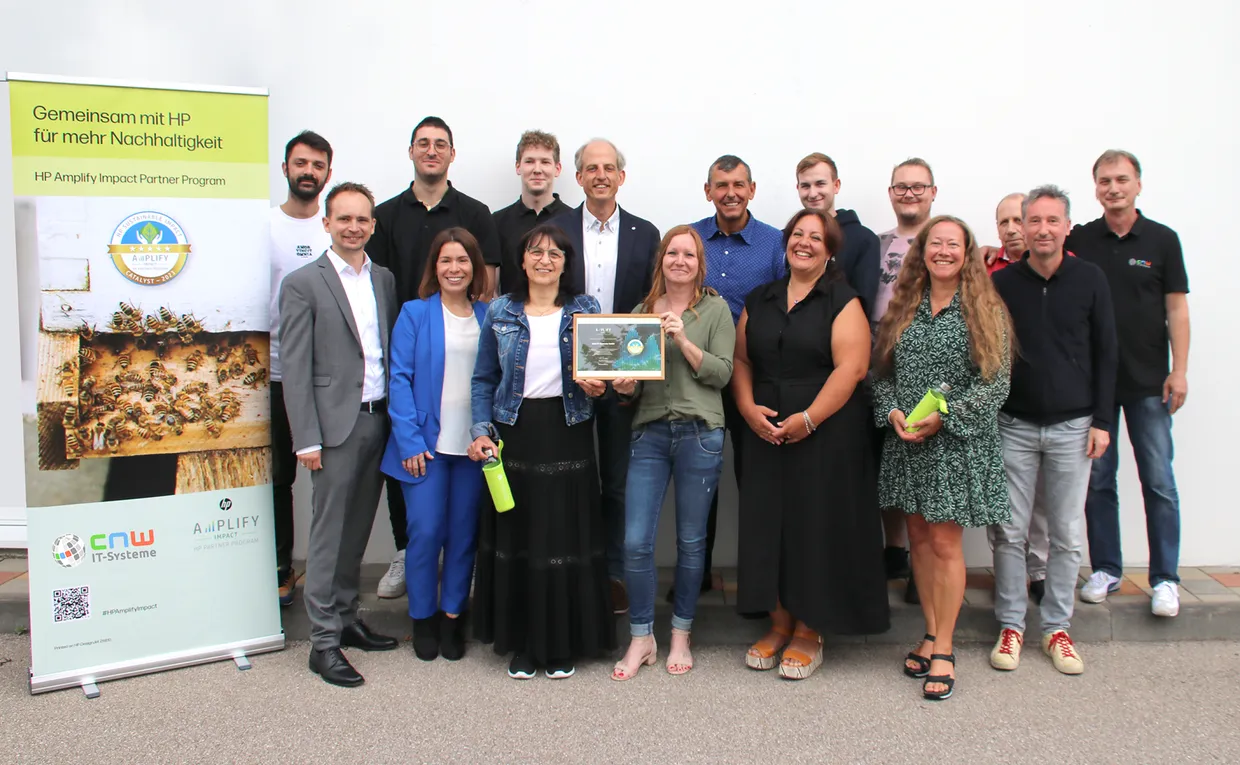 A group of 15 employees of CNW IT-Systeme smile at the camera and hold an award their company has won